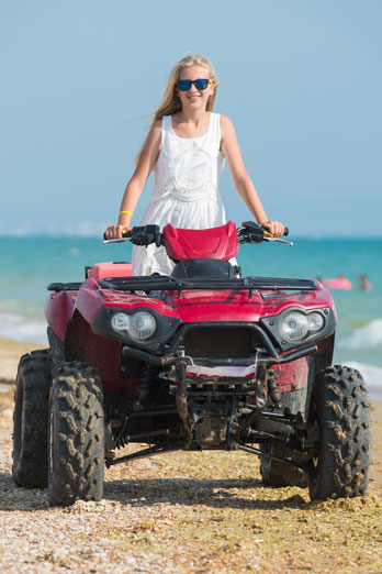 girl in sunglasses riding an atv on a beach